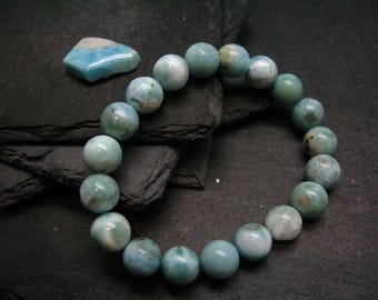 Puede incluir: Un brazalete de piedras preciosas azules y verdes con cuentas redondas. El brazalete está hecho de piedras naturales y tiene un acabado único e iridiscente.