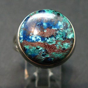 Puede incluir: Un anillo de plata con una gran piedra preciosa redonda de color azul, verde y marrón. La piedra preciosa tiene un patrón de remolino.