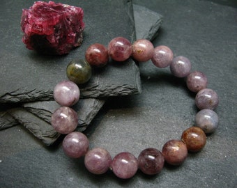 May include: A bracelet made of pink, purple, and green gemstone beads. The beads are round and have a smooth, polished finish.