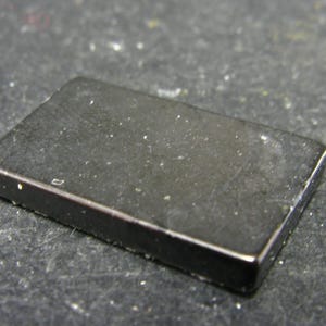 May include: A black rectangular magnet with a slightly textured surface.