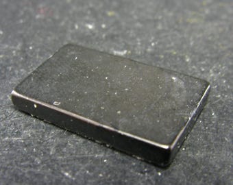 May include: A black rectangular magnet with a slightly textured surface.