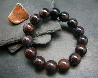 May include: A dark red gemstone bracelet with a high polish finish. The bracelet is made of round beads and is approximately 8 inches in length.