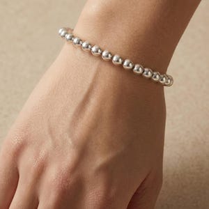 May include: A polished silver-tone beaded bracelet featuring a continuous row of uniform, spherical metallic beads strung together to form a circular band that rests comfortably around the wrist, showcasing a reflective and smooth surface finish.