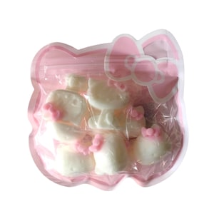 May include: A clear plastic bag shaped like a pink bow and a cat's head, filled with white, cat-shaped candies with pink bows. The candies are visible through the transparent packaging.