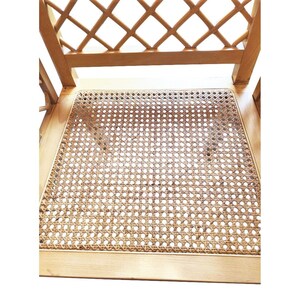 May include: Close-up of a wooden chair with a woven cane seat. The chair has a simple, elegant design with a lattice-like back.