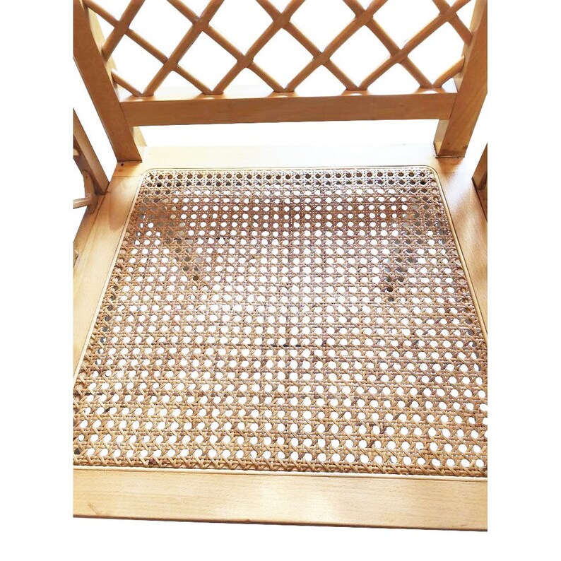 May include: Close-up of a wooden chair with a woven cane seat. The chair has a simple, elegant design with a lattice-like back.
