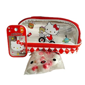 May include: A Hello Kitty themed set featuring a clear pencil case with a red trim, a small red case with Hello Kitty accessories, and a bag of Hello Kitty-shaped candies. The pencil case has a white background with Hello Kitty riding a bicycle.