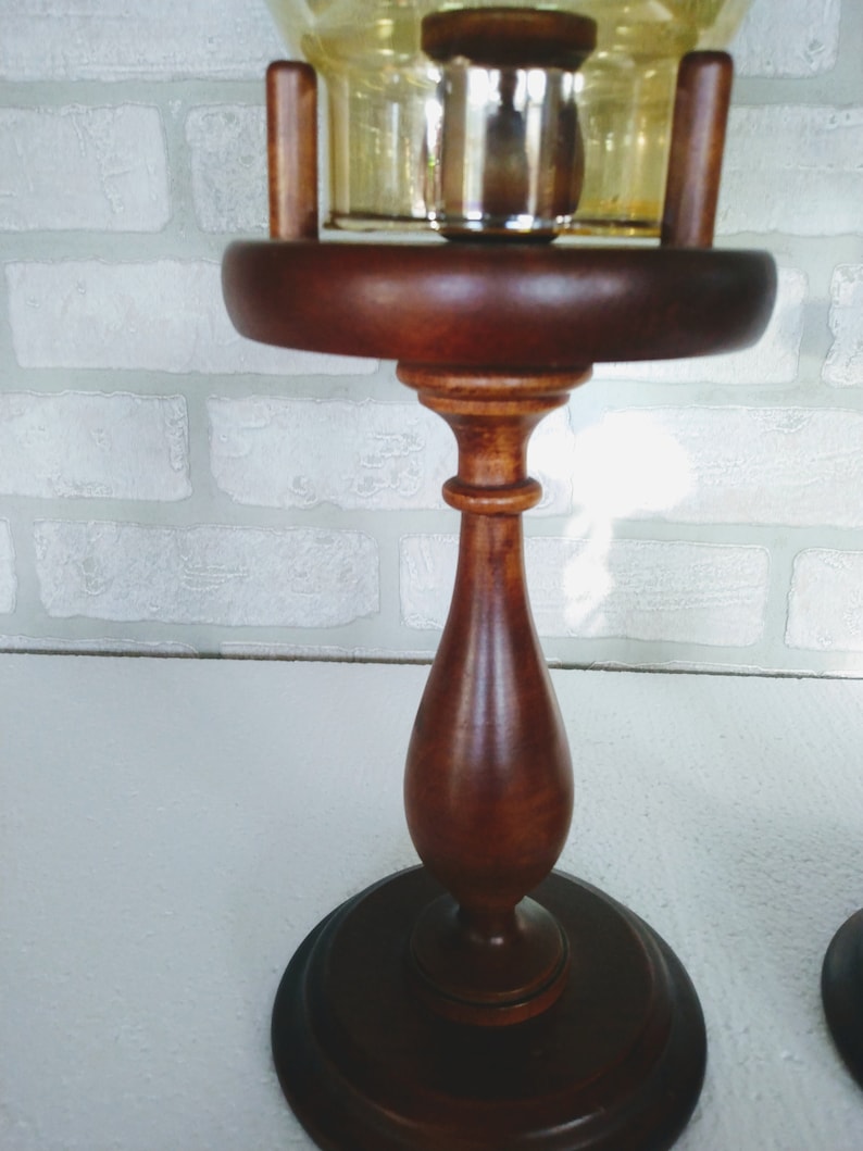 This image shows the wooden pedestal base with its elegant turned shape and polished medium-brown finish. The glass chimney sits securely above the base, supported by vertical wooden posts.
