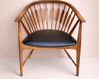 May include: A wooden armchair featuring a curved backrest with vertical, flattened spindles and a black upholstered seat. The frame is constructed from medium-toned wood with four legs and integrated armrests that flow into the backrest.
