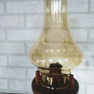A detailed view of the amber chimney showcases its rounded body and narrow neck with warm light reflecting off the surface. The bottom of the chimney fits into the wooden housing, showing the structural connection clearly.