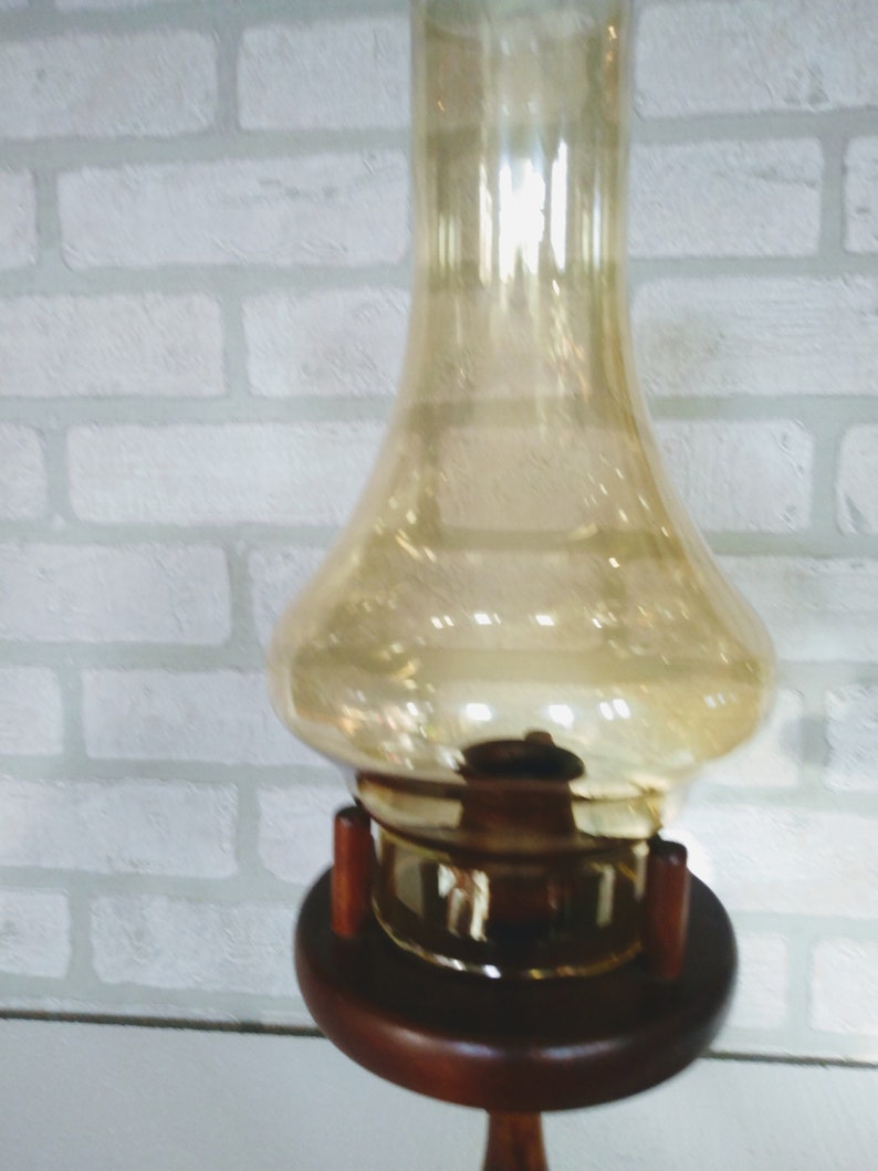 A detailed view of the amber chimney showcases its rounded body and narrow neck with warm light reflecting off the surface. The bottom of the chimney fits into the wooden housing, showing the structural connection clearly.