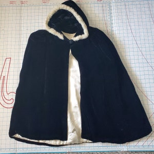 May include: A black velvet cape with a white faux fur collar. The cape has a long, flowing design and is perfect for adding a touch of elegance to any outfit.