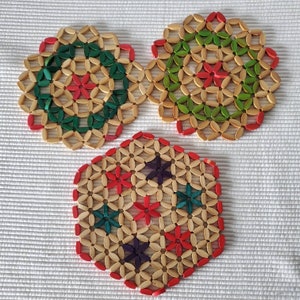 May include: Three round woven trivets with a floral design. The trivets are made of natural wood and feature red, green, and blue flowers.