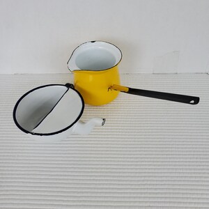 Peut inclure: Deux articles de cuisine en émail vintage. Un pichet jaune avec une poignée noire et un pichet blanc avec un bord bleu.