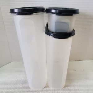 May include: Three clear plastic food storage containers with black lids. The containers are different sizes and shapes, with a tall, slender design. The containers are empty and ready to be filled with food.