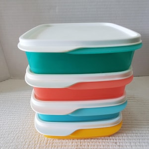 May include: A stack of colorful plastic food storage containers. The containers are rectangular with white lids and come in teal, coral, light blue, and yellow. The containers are stacked on top of each other.