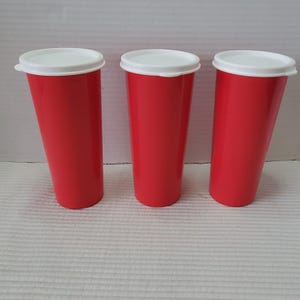 May include: Three red plastic tumblers with white lids are displayed against a white background. The tumblers are tall and cylindrical, with a slightly tapered shape. The lids fit snugly on top, creating a clean, modern look. These tumblers are ideal for cold beverages.