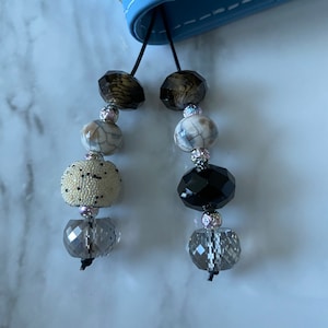 May include: Two beaded bookmarks with black cords. Each bookmark has a clear crystal bead, a black bead, a white and gray marbled bead, a brown and gold bead, and a white bead with black dots.
