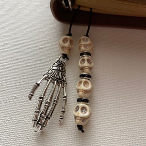 May include: Two black string bookmarks with white skull beads and a silver skeleton hand charm.