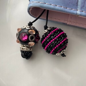 May include: Two black and pink beaded bookmarks with silver accents. One bookmark has a round bead with pink and clear rhinestones. The other bookmark has a long, oval bead with black and pink beads.