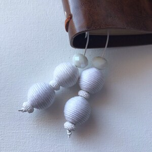 May include: White string beads with clear glass beads on a white background.