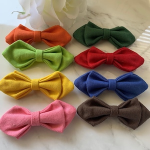 Può includere: Set di dieci papillon di diversi colori, tra cui arancione, verde, rosso, giallo, blu, rosa e marrone. I papillon sono realizzati in tessuto strutturato e hanno una forma a diamante.