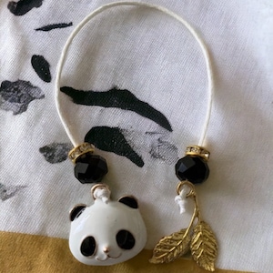 May include: A white panda charm with black eyes and a gold leaf charm on a white string with black beads.