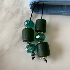 May include: A close-up of a green and silver beaded bookmark. The bookmark is attached to a blue notebook.