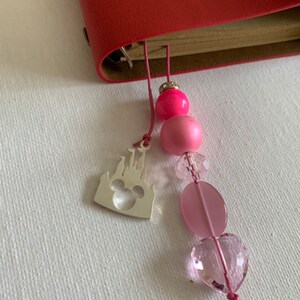 May include: A pink and clear glass beaded bookmark with a silver charm of the Disney castle and Mickey Mouse head.