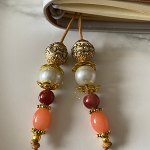 May include: Two gold and white beaded bookmarks with peach and brown beads hanging from them.