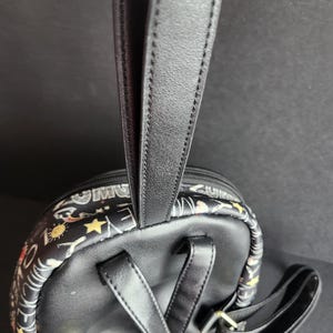 Peut inclure: Mini sac &agrave; dos noir avec une poign&eacute;e sup&eacute;rieure et des bretelles r&eacute;glables. Le sac &agrave; dos pr&eacute;sente un motif d'&eacute;toiles, de soleils et d'autres motifs. Les bretelles et la poign&eacute;e sont noires.