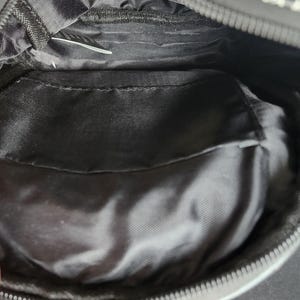Peut inclure: Sac en tissu noir avec fermeture &eacute;clair. L'int&eacute;rieur comporte une poche et une doublure lisse et brillante. L'ext&eacute;rieur du sac pr&eacute;sente un motif noir et blanc. Le sac est ouvert, r&eacute;v&eacute;lant l'int&eacute;rieur.