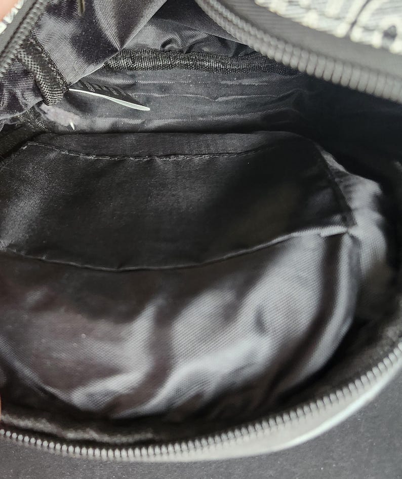 Peut inclure: Sac en tissu noir avec fermeture &eacute;clair. L'int&eacute;rieur comporte une poche et une doublure lisse et brillante. L'ext&eacute;rieur du sac pr&eacute;sente un motif noir et blanc. Le sac est ouvert, r&eacute;v&eacute;lant l'int&eacute;rieur.