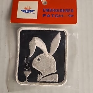 Peut inclure: Écusson brodé avec un motif de lapin blanc et un verre à martini sur un fond noir, bordé de blanc. L'écusson est attaché à une étiquette rouge avec le texte "EMBROIDERED PATCH".