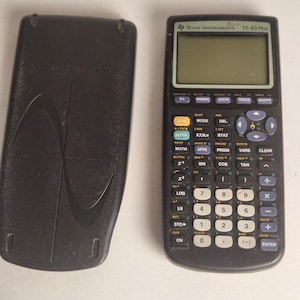 May include: A black Texas Instruments TI-83 Plus graphing calculator with its protective cover. The calculator has a screen, numerous buttons, and the text "Texas Instruments TI-83 Plus" printed on the top. The cover is black and has a curved design.