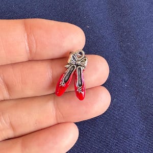 May include: A silver charm in the shape of a pair of red ballet shoes with a silver bow.