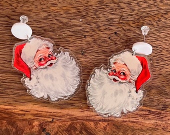 May include: A pair of festive earrings featuring a vintage Santa Claus design. Each earring showcases a smiling Santa face with a red hat and white beard, paired with a white circular accent. Ideal for Christmas celebrations.
