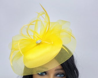 May include: A yellow fascinator hat with a small, clear rhinestone embellishment. The hat is made of a soft, sheer fabric and has a delicate, feminine design.