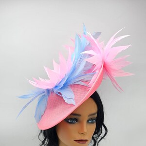 Könnte beinhalten: Ein rosa und blauer Federhut mit breiter Krempe. Der Hut sitzt auf einem Mannequin-Kopf.