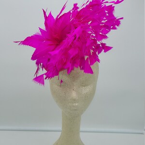 May include: A bright pink feather headpiece on a white mannequin head. The feathers are arranged in a circular shape and are very full.