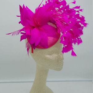 May include: A bright pink fascinator with a large flower and feathers.