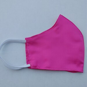 May include: A pink face mask with white elastic straps. The mask is made of a soft, smooth fabric.