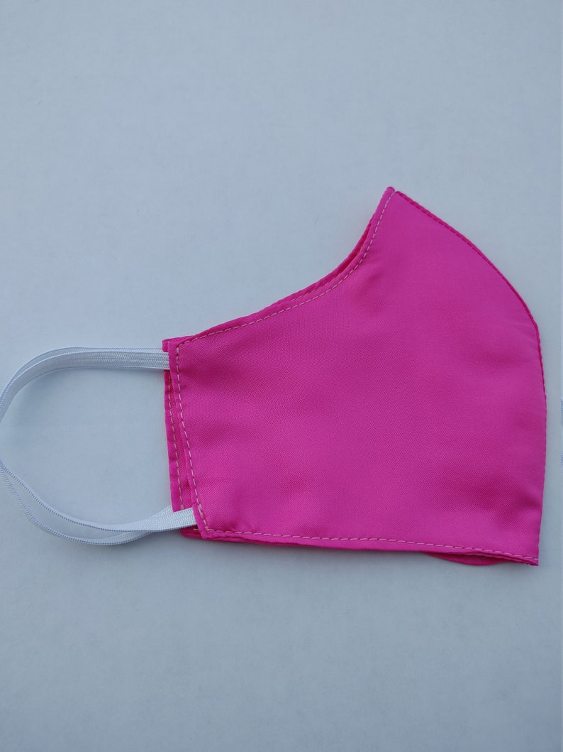 May include: A pink face mask with white elastic straps. The mask is made of a soft, smooth fabric.