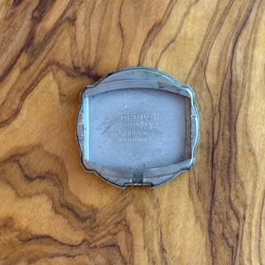 May include: A vintage silver-toned watch case with a rectangular interior. The case features a curved, decorative design around the edges. The back of the watch case has engraved text, including the number H508305.