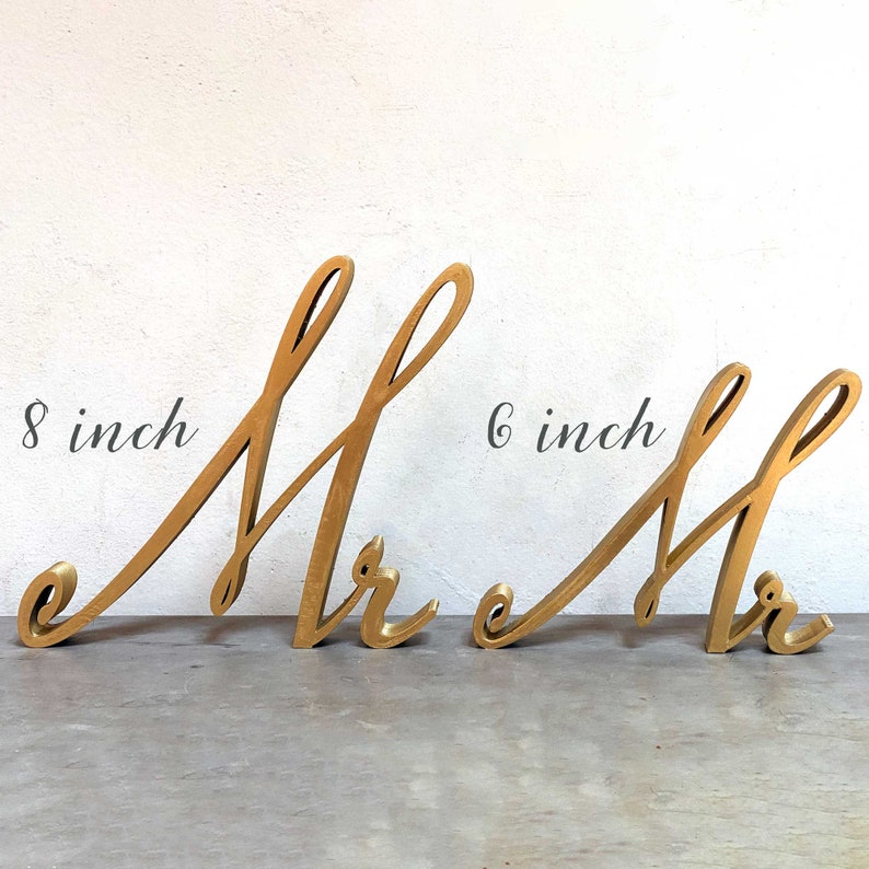 May include: Two gold-colored wooden letters, "Mr", in a cursive script font. The left letter is 8 inches tall and the right letter is 6 inches tall.