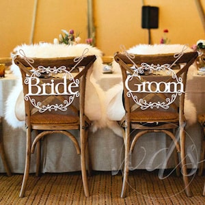 May include: Two wooden chairs with white faux fur seat cushions and decorative signs that say "Bride" and "Groom" attached to the back of the chairs.