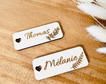 Marcador de lugar para boda en madera clara personalizable con los nombres de los invitados grabados estilo bautizo boho chic con pequeño agujero en forma de corazón natural