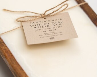 Op de afbeelding: Een bruin papieren label vastgebonden met touw met de tekst "HUNTER'S HOPE WINTER PARK WHITE OAK biologische sojawas kaars 16-36 OZ Handgemaakt in Colorado Springs, Colorado MADE WITH MEANING".