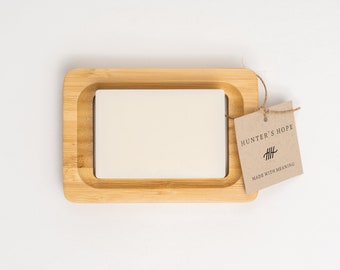 Op de afbeelding: Een houten dienblad met een witte vierkante tegel erin. Een bruin papieren label is met een touwtje aan het dienblad bevestigd. Het label zegt "Hunter's Hope" en "HHH" met de tekst "Made with Meaning" eronder.