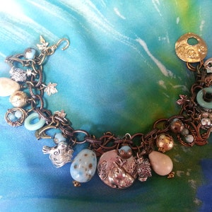 May include: A charm bracelet with a copper chain and various charms, including a bird, a nest, a leaf, a squirrel, and a heart. The charms are silver and gold toned.